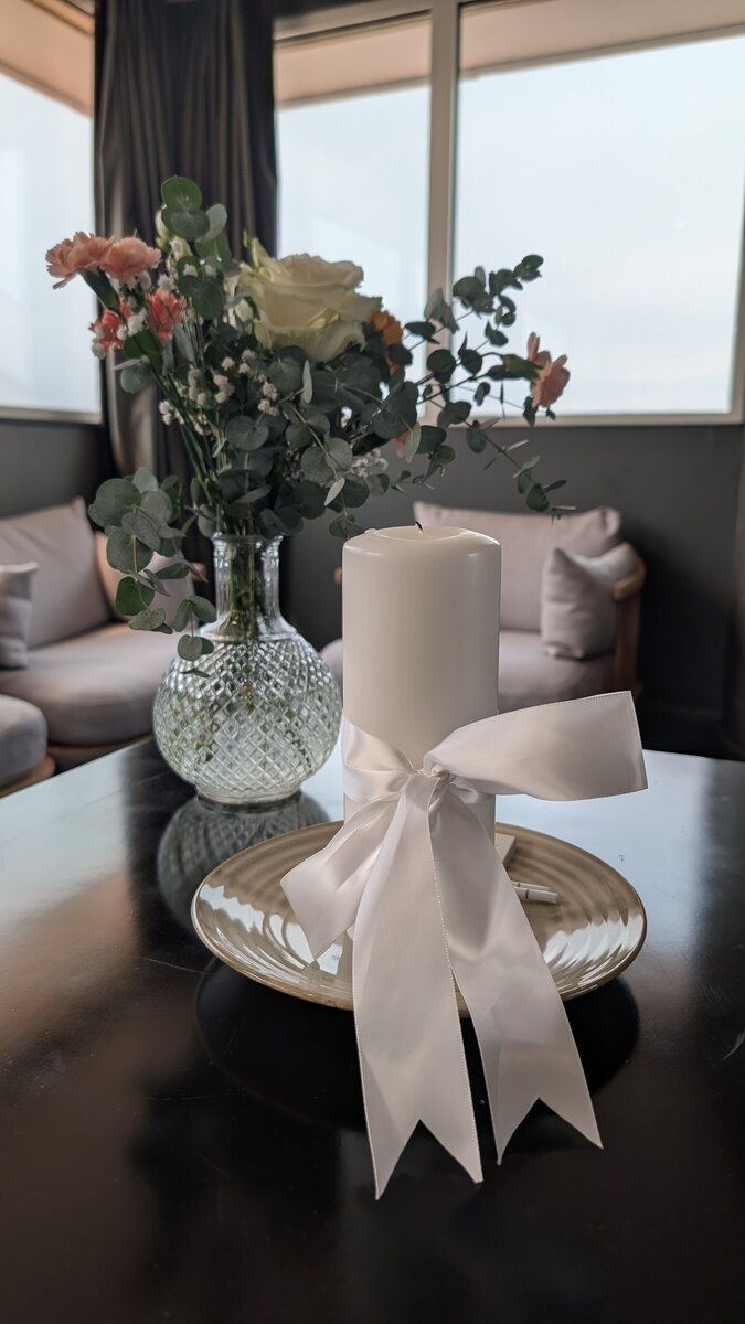 Bougie blanche nouée d'un ruban de satin, accompagnée d'un vase de fleurs