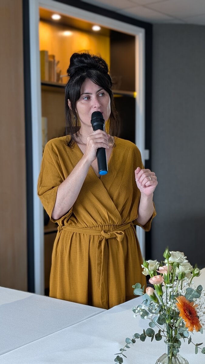 Mylène Chevreul tenant un micro lors d'une cérémonie, près d'un bouquet de fleurs