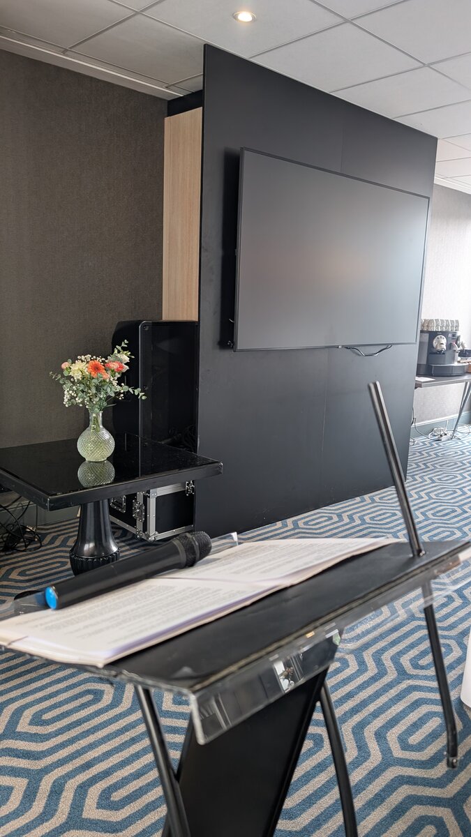 Pupitre de conférence vide dans une salle, avec un écran et un bouquet de fleurs en arrière-plan, attendant que la parole soit portée