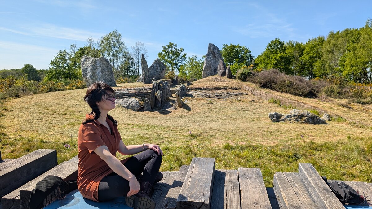 Mylène Chevreul en méditation, assise sur un banc en bois face aux pierres dressées de Saint-Just en Bretagne